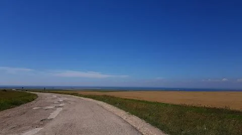 A dirt road through the fields leads to the sea. clear skies in sunny weather Stock Photos