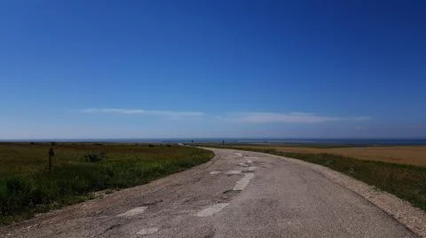 A dirt road through the fields leads to the sea. clear skies in sunny weather Stock Photos