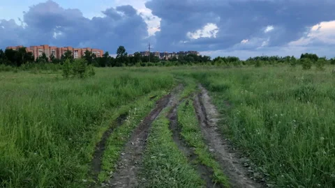 Dirt road through green field under cloudy sky in summer evening Stock Footage 155372914