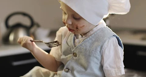 A dirty boy in a culinary cap eats chocolate with a fork in the kitchen. Stock Footage 85818751