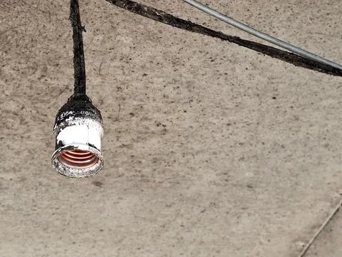 A dirty, broken light bulb socket hanging from a grimy ceiling with exposed.. Stock Photos