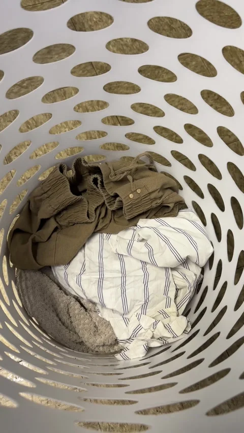 Dirty clothes being placed into a laundry basket vertical photo Stock Footage 342977929