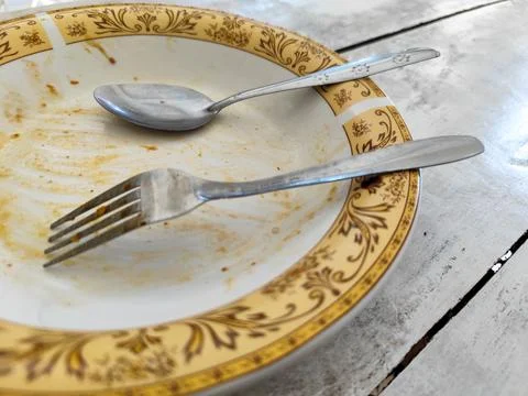 Dirty empty plate with fork and spoon after meal on rustic wooden table Stockfoto's