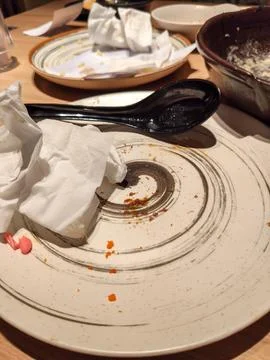 Dirty Empty Plates with Leftover Food and Used Napkins on Dining Table Stock Photos