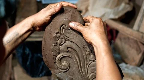 Dirty hands of worker making clay statue in Balinese style in dark workshop Stock Photos