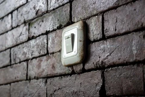 A dirty light switch mounted on an old brick wall. Stock Photos