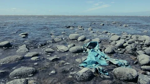 A dirty old piece of blue polluting plastic litter, washed up onto some rocks Stock Footage 77350147