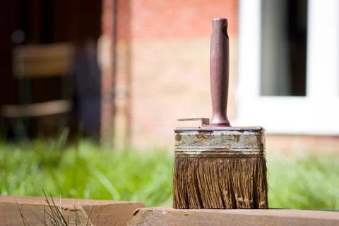 Dirty red paint brush lying on piece of wood after work, landscaping, garden 库存照片