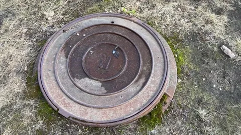 A dirty rusty iron hatch with a pattern is located next to dry grass during the Stock Footage 270425827