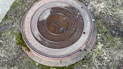 A dirty rusty iron hatch with a pattern is located next to dry grass during the Stock Footage 270425874