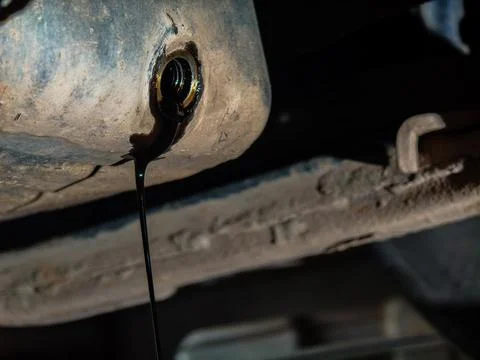 Dirty used engine oil draining from the open drain plug of an automotive oil pan Stock Photos