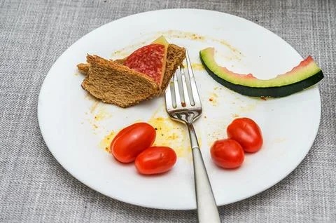 Dirty white plate with leftover bread, salami, tomatoes, and watermelon rind 写真素材