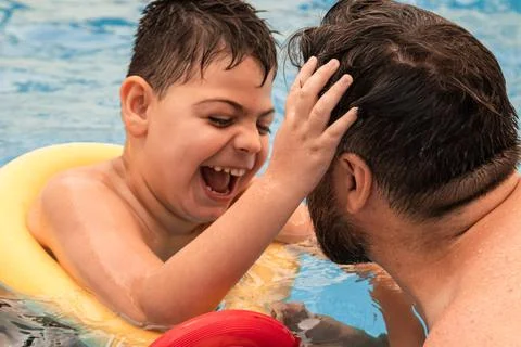 Disabled boy with a float laughs as he plays and swims in a pool with his father Stock Photos