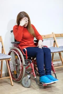 Disabled crying woman in wheel-chair covers her face with hand while sitting  Foto stock
