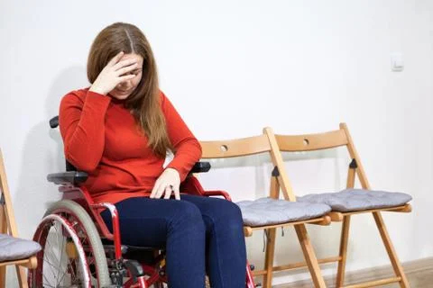 Disabled crying woman in wheelchair covers her face with hand while sitting b 写真素材