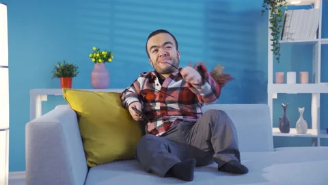Disabled dwarf young man resting on sofa at home and looking at his smartphone. Stock Footage 230974340