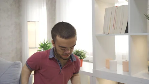 Disabled dwarf young man takes books from the shelf at home  Stock Footage 230969227