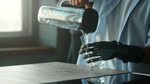 Disabled guy with bio hand prothesis pours water into glass Stock Footage 157350116