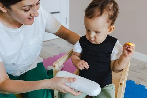 Disabled kid practicing sitting posture in special supportive chair at home. Stock Photos