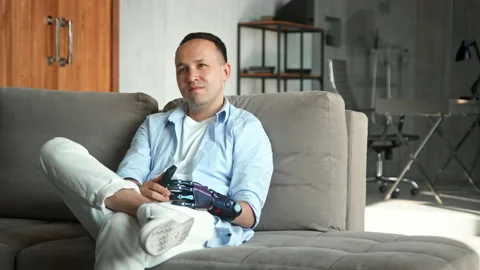 Disabled man with bio hand prothesis switches television Stock Footage 157348529