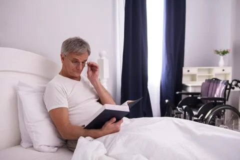 Disabled man reading in bed. Stock Photos
