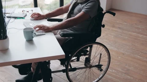 Disabled man sitting in wheelchair at the table in front of computer Stock Footage 231707441