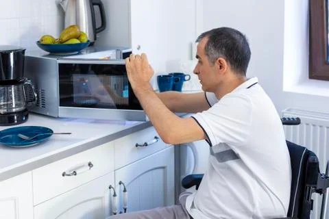 Disabled Man Using Microwave Oven For Baking In Kitchen Stockfoto's
