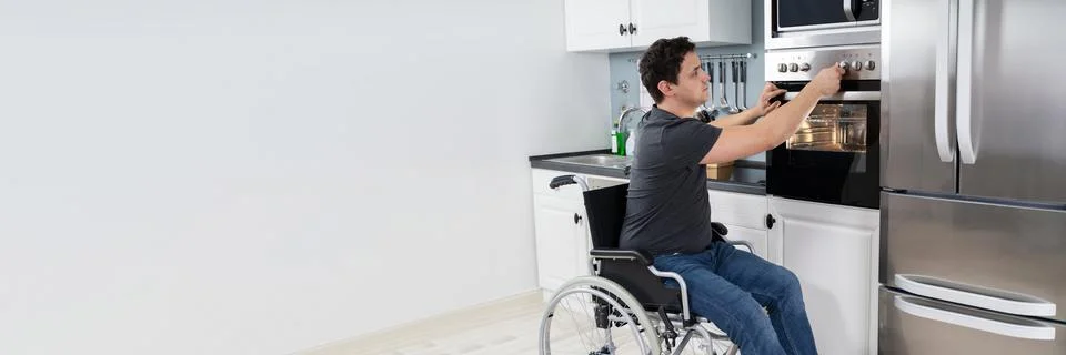 Disabled Man Using Microwave Oven In Kitchen Stock Photos