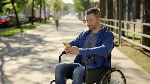 Disabled man, using smartphone sitting on the wheel chair in the street near Stock Footage 212005264