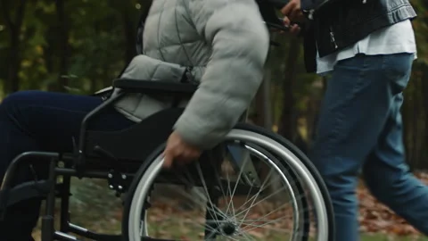Disabled man vigorously pushes the wheels of a wheelchair while a person walks Stock Footage 255552451
