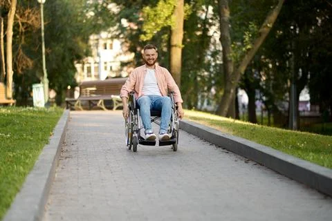 Disabled man in wheelchair rides on a path in park Stock Photos