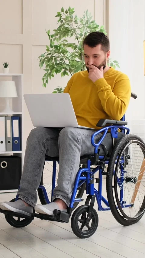 Disabled man in a wheelchair thoughtfully working on a laptop at home. Stock Footage 328122729