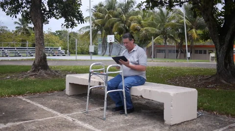 DISABLED-PARAPLEGIC: old man on park bench with Ipad-tablet walking frame Stock Footage 51069884