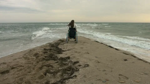 The disabled person gets out of the stroller on the shore of the sea Stock Footage 95218894