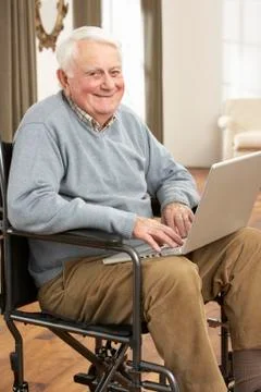 Disabled Senior Man Sitting In Wheelchair Using Laptop Stock Photos