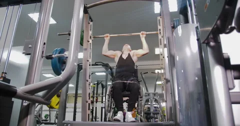 Disabled wheelchair user performs pull-ups on the horizontal bar. Gym workout. Stock Footage 146764778