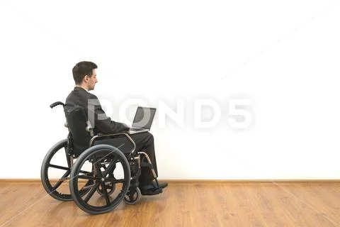 The disabled in a wheelchair works with a laptop on the white wall background Stock Photos