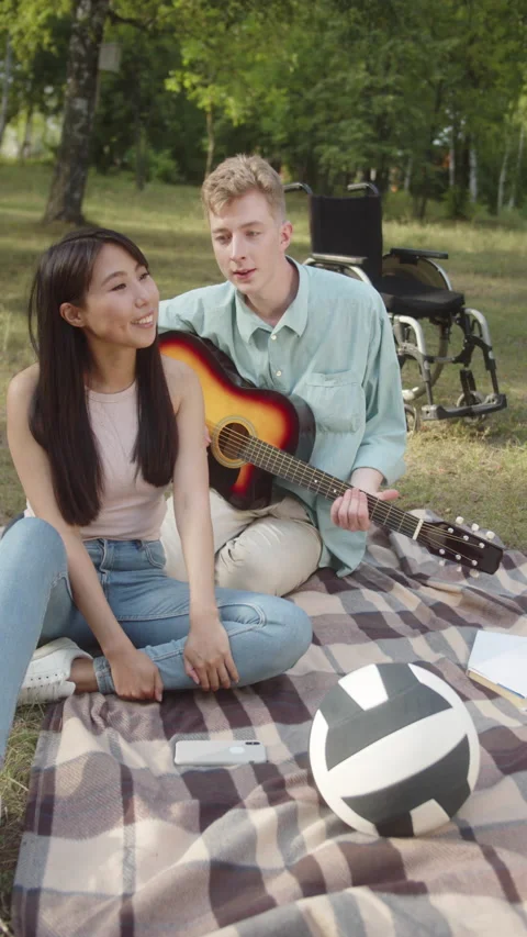 A disabled young guy in a blue shirt is playing guitar and singing songs for his Stock Footage 173945146