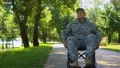 Disabled young man in military uniform moving in wheelchair in city park, injury 4k or 4k+ Resolution
