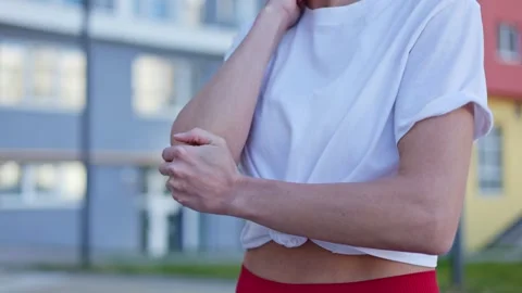 Disappointed female touching elbow while standing on pedestrian street 스톡 동영상 276454892