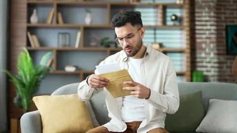 Disappointed handsome man reading letter with bad news sitting on sofa at home.  Stock Footage 288499386