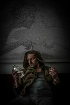 Disappointed man with a hood and empty engraved glass bottle of alcohol Stock Photos
