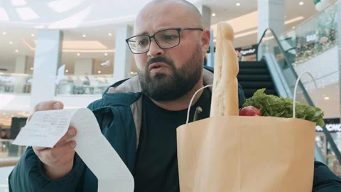 Disappointed plus size man with shopping paper bag full of food looks at sale Stock Footage 265898366
