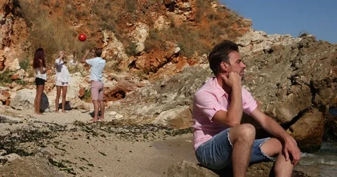 Disappointed Sad Man Sitting Far Group of Young People Playing Beach Volleyball Stock Footage 77006901