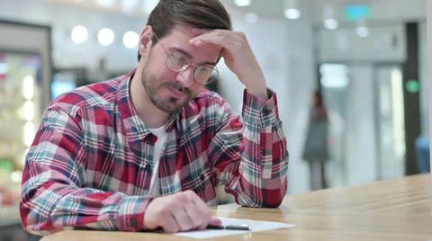 Disappointed Young Man Trying to Write on Paper in Cafe Foto stock