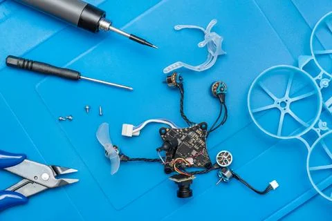 Disassembled micro FPV tiny whoop drone and repair tools on blue mat Foto stock