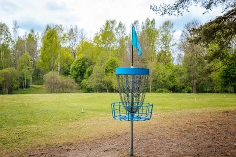 Disc golf basket with blue flag positioned on a grassy field surrounded by .. Stock Photos