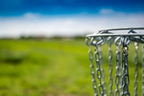 Disc golf goal chains gently swaying in the breeze with a green course in the Stock Photos