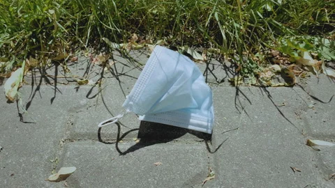 Discarded face mask on the ground. Impact on environmental plastic pollution. Stock Footage 155352181