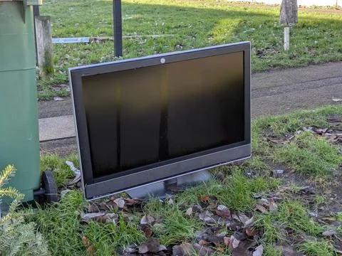Discarded Flat Screen Television Dumped on Grass Verge Next to Public Trash B Stock Photos